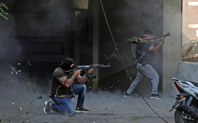 Shiite fighters from Hezbollah and Amal movements take aim with (L to R) a Kalashnikov assault rifle and a rocket-propelled grenade launcher amidst clashes in the area of Tayouneh, in the southern suburb of the capital Beirut, on October 14, 2021. Gunfire killed several people and wounded 20 at a Beirut rally organised by the Shiite Hezbollah and Amal movements to demand the dismissal of the Beirut blast lead investigator, the state-run National News Agency said. (Photo by Ibrahim Amro/AFP Photo)
