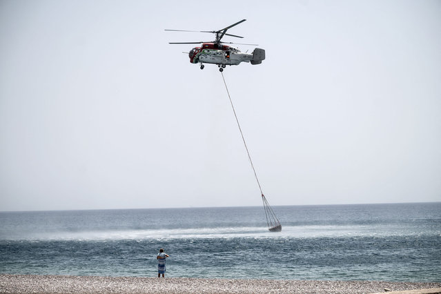 A helicopter scoops water from the sea to douse wildfires, close to the beach near the village of Gennadi, in the southern part of the Greek island of Rhodes, on July 27, 2023. Wildfires have been raging in Greece amid scorching temperatures, forcing mass evacuations in several tourist spots including on the islands of Rhodes and Corfu. (Photo by Angelos Tzortzinis/AFP Photo)