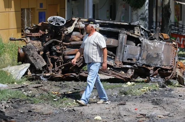 A local resident walks past a destroyed vehicle during Ukraine-Russia conflict in the city of Lysychansk in the Luhansk Region, Ukraine on July 4, 2022. (Photo by Alexander Ermochenko/Reuters)