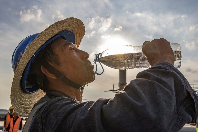 In this photo released by Xinhua News Agency, a worker drinks at the construction site of the T3B terminal project of Chongqing Jiangbei International Airport in southwest China's Chongqing, July 11, 2022. Flooding and extreme high temperatures have caused multiple deaths in eastern China as summer heat descends earlier than usual. (Photo by Huang Wei/Xinhua via AP Photo)
