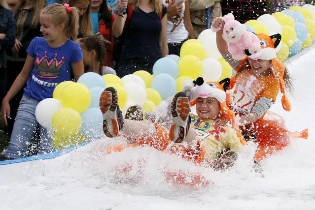 Children slide down on a float along a chute to cross a pool of water and foam during the “Letniy Gornoluzhnik” (Summer mountain puddle rider) festival at the Bobroviy Log Fun Park near the Siberian city of Krasnoyarsk, Russia, August 23, 2015. (Photo by Ilya Naymushin/Reuters)