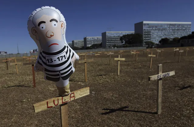 In this August 27, 2017 photo, a doll representing Brazil's President Luiz Inacio Lula da Silva wearing prison clothes stands on a cross with his name in Brasilia, Brazil. Demonstrators placed crosses representing the death of corrupt politicians. In July, Lula was found guilty of corruption and money laundering and sentenced to almost 10 years in prison. Now his case goes before a group of magistrates. (Photo by Eraldo Peres/AP Photo)
