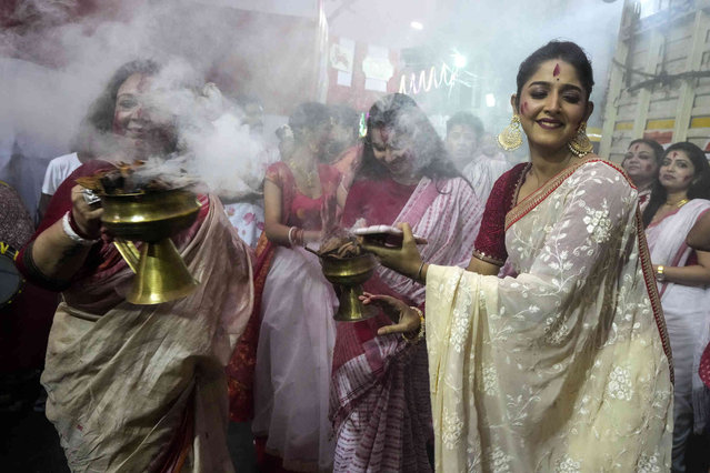 Women dabce in front of an idol of Hindu goddess Durga before it is immersed in the Hooghly River in Kolkata, India, Tuesday, October 24, 2023. The immersion of idols marks the end of the festival that commemorates the slaying of a demon king by lion-riding, 10-armed goddess Durga, marking the triumph of good over evil. (Photo by Bikas Das/AP Photo)