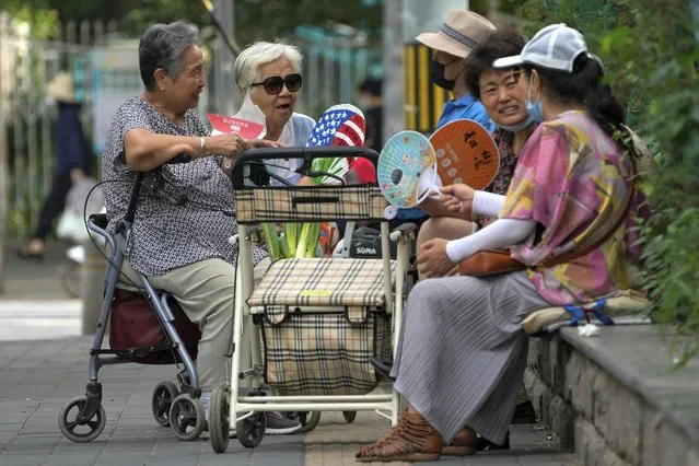 Residents fan themselves as they chat with each other outside a residential complex in Beijing, Sunday, August 21, 2022. (Photo by Andy Wong/AP Photo)