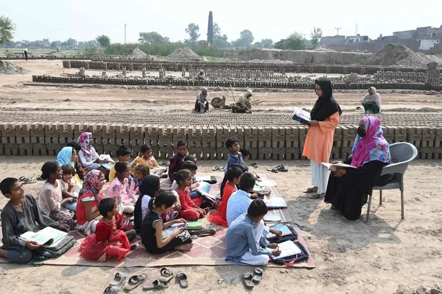 Children of brick kiln workers attend a class at a brick kiln site in Lahore on September 8, 2022. (Photo by Arif Ali/AFP Photo)