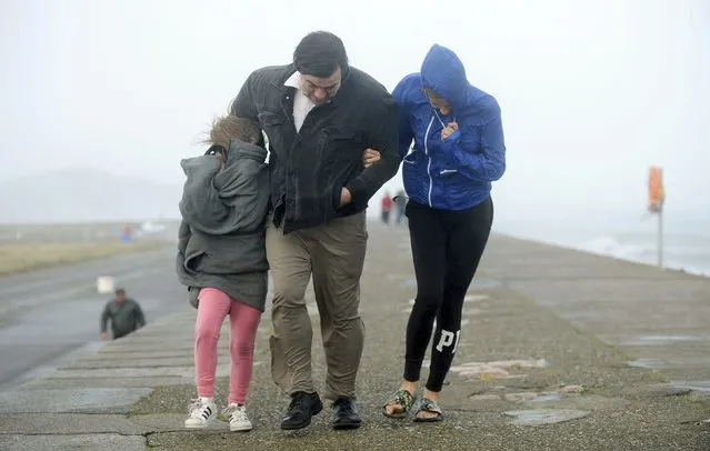 A family walks along a seawall during storm Ophelia on East Pier in Howth, Dublin, Ireland, as the remnants of Hurricane Ophelia batter Ireland and the United Kingdom with gusts of up to 80mph (129kph), Monday October 16, 2017. Three people have been confirmed dead in Ireland in incidents related to Storm Ophelia. (Photo by Caroline Quinn/PA Wire via AP Photo)