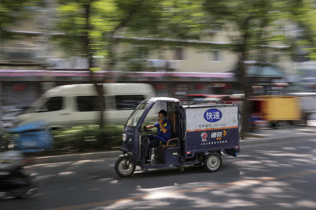 A private delivery company's courier wearing a protective face mask to help curb the spread of the new coronavirus rides his delivery cart passes by a residential area in Beijing, Sunday, June 21, 2020. According to state media reports, nearly one hundred thousand delivery workers have to accept the nucleic acid testing, a countermeasure to prevent the spread of the virus in the capital city. (Photo by Andy Wong/AP Photo)