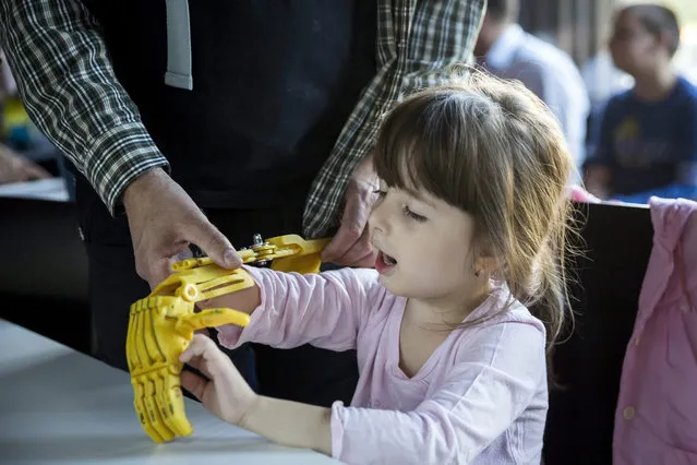 A Hungarian girl tries a 3D-printed prosthetic hand, made for her during the presentation of the e-NABLE voluntary team in the glass pavilon of the Design Terminal in Budapest, Hungary, 21 September 2015. E-Nable is a worldwide, network of inventors and designers, which use 3D printing process to make functional, assistive hands for people in need. (Photo by Balazs Mohai/EPA)