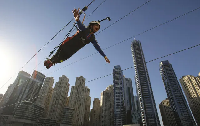 A woman rides the world's longest urban zip line, with a speed of up to 80 kilometers per hour on a one kilometer run from 170 meter to ground level, in the Marina district of Dubai, United Arab Emirates, Tuesday, December 5, 2017. (Photo by Kamran Jebreili/AP Photo)