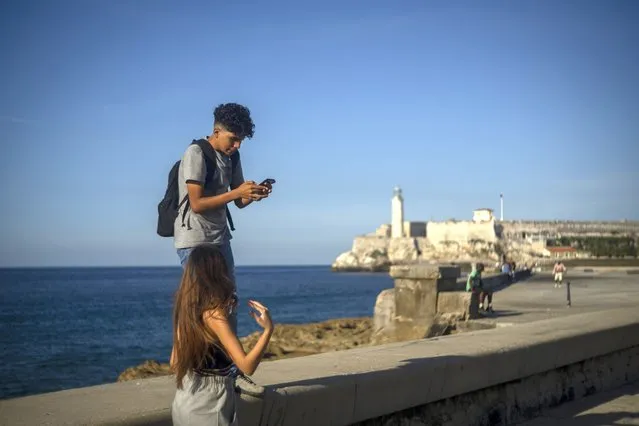 A youth uses his smartphone as he and a friend walk along the Malecon seawall in Havana, Cuba, Friday, November 25, 2022. Ever-widening access to the internet is offering a new opportunity for Cubans looking for hard-to-obtain basic goods: online shopping. (Photo by Ramon Espinosa/AP Photo)