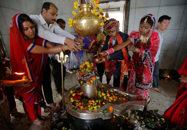 A newly-married couple and other Hindu devotees pour holy water over a Shivling (a symbol of Lord Shiva) as they pray inside a temple during the Maha Shivaratri festival in Kolkata, February 13, 2018. (Photo by Rupak De Chowdhuri/Reuters)