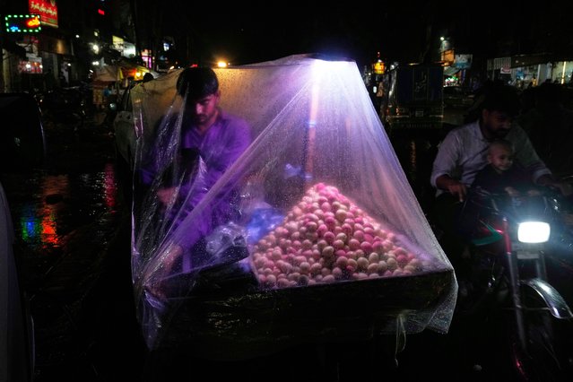A road side vendor waits for a customer with a plastic sheet over him to protect himself from rain in Lahore, Pakistan, Tuesday, July 15, 2025. (Photo by K.M. Chaudary/AP Photo)