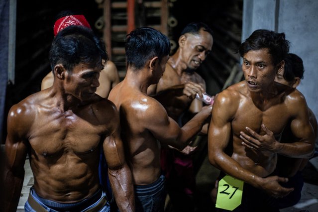 This photo taken on August 11, 2025 shows roof tile factory workers smear each other's bodies with oil before taking part in a traditional bodybuilding competition at a roof tile factory in Jatiwangi, West Java. This is a bodybuilding battle of a different kind – one where competitors are roof tile factory workers who pump clay instead of iron to bring attention to their dwindling trade. In Java's Jatiwangi city, an Indonesian hub for clay roof tile production nearly 200 kilometres from capital Jakarta, dozens of men have been lathering on oil to pose for crowds since 2015 to show they are not going anywhere. (Photo by Aditya Irawan/AFP Photo)