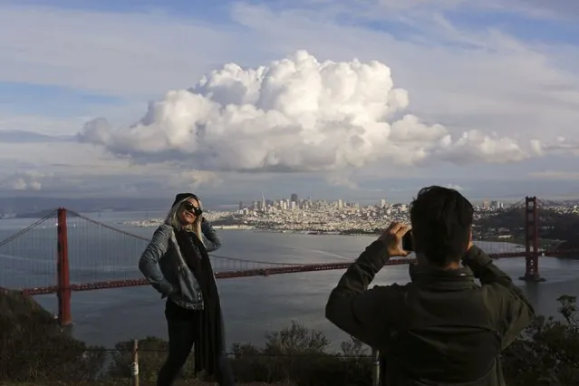 Visitors to the Marin Headlands pose for photographs overlooking the Golden Gate Bridge and skyline of San Francisco, as a large cloud gathers over the city, December 12, 2014. A major storm pummeled California and the Pacific Northwest with heavy rain and high winds on Thursday, killing one man, knocking out power to tens of thousands of homes, disrupting flights and prompting schools to close. (Photo by Robert Galbraith/Reuters)