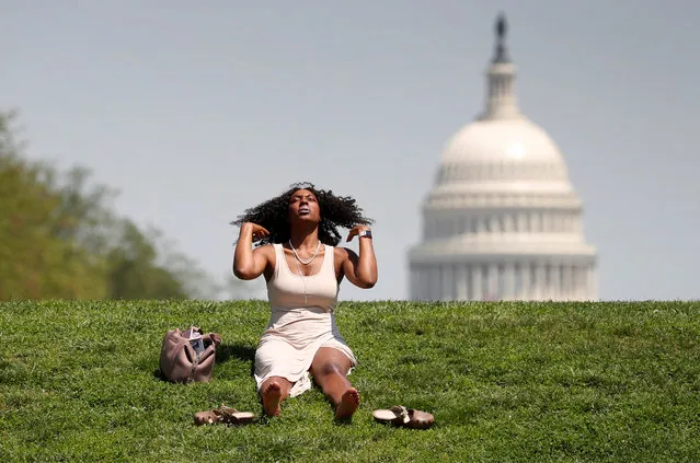 With the U.S. Capitol in the background, Kellye Sims flips her hair up as she basks in the sun, at the National Mall, during a record-setting heat wave in Washington, D.C. on May 3, 2018. (Photo by Kevin Lamarque/Reuters)