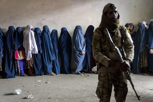 A Taliban fighter stands guard as women wait to receive food rations distributed by a humanitarian aid group, in Kabul, Afghanistan, Tuesday, May 23, 2023. (Photo by Ebrahim Noroozi/AP Photo)