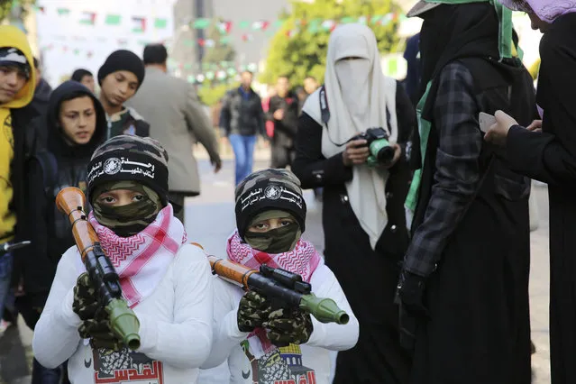 Palestinian children cover their faces as they carry toy weapons, during a rally to commemorate the 28th anniversary of the Hamas militant group, at the main road in Gaza City, Monday, December 14, 2015. The Arabic on their headbands reads, “no God but Allah and Muhammad is his messenger. Izzedine al-Qassam Brigades”. (Photo by Adel Hana/AP Photo)