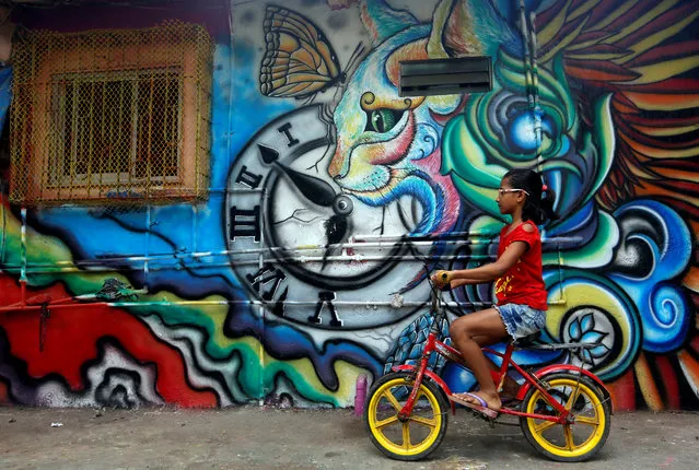 A girl rides her cycle past a decorated wall of a house at a slum in Mumbai, India, May 24, 2018. (Photo by Francis Mascarenhas/Reuters)