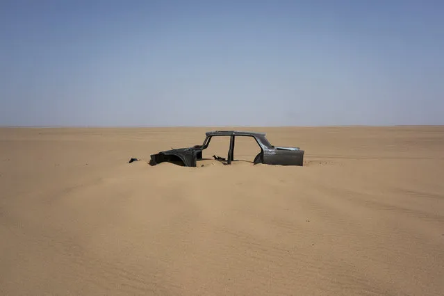 The frame of an abandoned Peugeot 404 rests in Niger's Tenere desert region of the south central Sahara on Sunday, June 3, 2018. Once a well-worn roadway for overlander tourists, the highway’s 4,500 kilometers (2,800 miles) are a favored path for migrants heading north in hopes of a better life – and more recently thousands who are being expelled south from Algeria. (Photo by Jerome Delay/AP Photo)