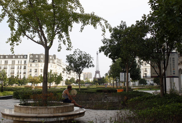 A man sits under a tree at the Tianducheng development in Hangzhou, Zhejiang Province August 1, 2013. Tianducheng, developed by Zhejiang Guangsha Co. Ltd., started construction in 2007 and was known as a knockoff of Paris with a scaled replica of the Eiffel Tower standing at 108 metres (354 ft) and Parisian houses. Although designed to accommodate at least 10 thousand people, Tianducheng remains sparsely populated and is now considered as a “ghost town”, according to local media. (Photo by Aly Song/Reuters)