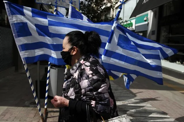 A woman wearing a face mask against the spread of coronavirus, walks in front of Greek flags which are for sale in Athens, Friday, March 19, 2021. The military parade on March 25, marking 200-years since the war that resulted in Greece's independence from the Ottoman Empire and rebirth as a nation, will be held without spectators due to the coronavirus, and only Greek and foreigners political officials will attend it. (Photo by Thanassis Stavrakis/AP Photo)