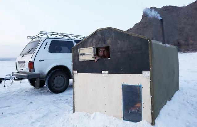 Fisherman Alexander Romantsov looks out of the window of his plywood lodge, placed on the frozen surface of the Yenisei River over an ice hole for fishing at the beginning of winter, near the village of Anash, Novosyolovsky District of Krasnoyarsk region, Russia February 7, 2015. Some fishermen of the region equip such tiny lodges with mini coal and firewood-burning ovens and also install electricity taken from car accumulator batteries, which allow them to fish day and night in spite of severe frost. (Photo by Ilya Naymushin/Reuters)