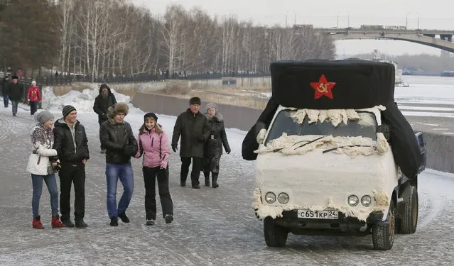 Pedestrians walk past a truck with a giant Soviet Red Army hat seen on it, an installation created by Russian artist Vasily Slonov, during the annual “Winter Virage” motor sports festival dedicated to the Defender of the Fatherland Day on the embankment of the Yenisei River in Russia's Siberian city of Krasnoyarsk, February 23, 2015. (Photo by Ilya Naymushin/Reuters)