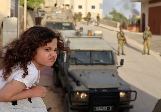 A Palestinian girl watches from the balcony of her house as Israeli soldiers conduct a security operation in the village of Aqraba, east of Nablus in the occupied-West Bank, on May 3, 2021. Suspected Palestinian gunmen carried out a drive-by shooting at a nearby junction the previous, leaving three Israeli civilians wounded, one of them in critical condition, with a manhunt underway. (Photo by Jaafar Ashtiyeh/AFP Photo)