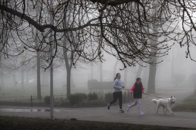 A mother and daughter run on a foggy morning at the Cathedral square in Vilnius, Lithuania, Monday, April 10, 2023. The air temperature in the morning is 6 degrees Celsius (42,8 degrees Fahrenheit). (Photo by Mindaugas Kulbis/AP Photo)