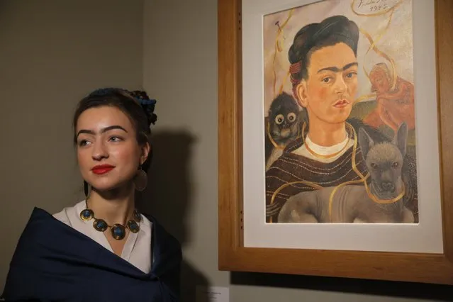 A visitor stylised as Frida Kahlo poses for photo next to a Frida's Kahlo self-portrait at the Frida Kahlo exhibition in St.Petersburg, Russia, Tuesday, February 2, 2016. A retrospective exhibition of the renowned Mexican artist Frida Kahlo started on Tuesday at the Faberge Museum. This is the first Frida Kahlo exposition of such scale in Russia. The exhibition features 34 works, including paintings, drawings and lithographs. (Photo by Dmitry Lovetsky/AP Photo)