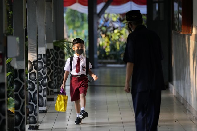 Staff greets a student during the first day of school reopening at an elementary school in Jakarta, Indonesia, Monday, August 30, 2021. Authorities in Indonesia's capital kicked off the school reopening after over a year of remote learning on Monday as the daily count of new COVID-19 cases continues to decline. (Photo by Dita Alangkara/AP Photo)