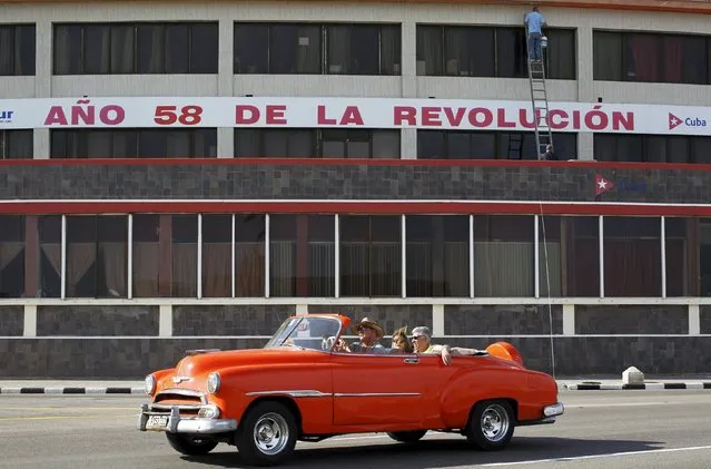 Foreign visitors drive past a sign reading “58th year of the Revolution” in Havana, March 17, 2016. (Photo by Reuters/Stringer)