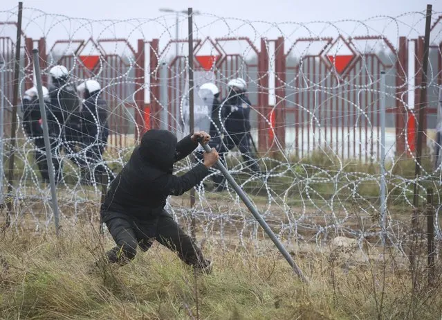 A man pulls down the fence during clashes with Polish border guards at the Belarus-Poland border near Grodno, Belarus, on Tuesday, November 16, 2021. Polish border forces say they were attacked with stones by migrants at the border with Belarus and responded with a water cannon. The Border Guard agency posted video on Twitter showing the water cannon being directed across the border at a group of migrants in a makeshift camp. (Photo by Leonid Shcheglov/BelTA via AP Photo)