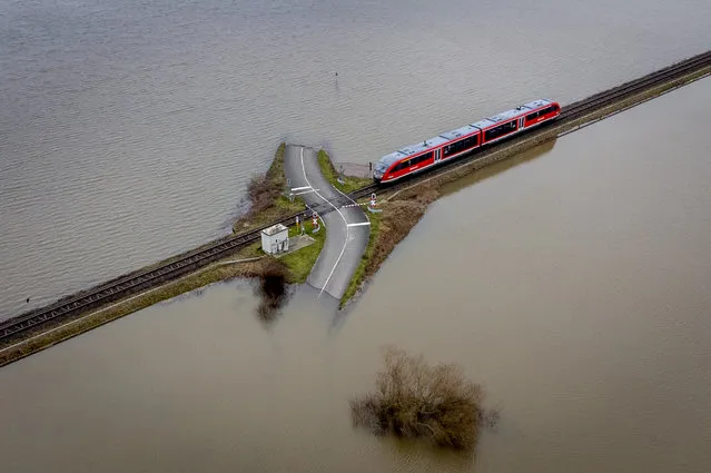 A regional train approaches passes a railroad crossing between flooded fields in Nidderau-Eichen near Frankfurt, Germany, Monday, January 16, 2023. (Photo by Michael Probst/AP Photo)