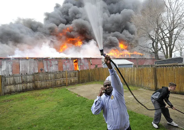 Greg Garmon, Sr. uses a garden hose to wet the side of his house in Erie, Pa., as a warehouse fire rages in the background on Monday, April 11, 2016. Multiple fire crews responded to the fire. (Photo by Christopher Millette/Erie Times-News via AP Photo)