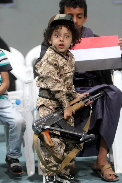 A boy looks on while holding a rifle and attending celebrations with his brother marking the 25th anniversary of Yemen's unification in Sanaa May 23, 2015. (Photo by Mohamed al-Sayaghi/Reuters)