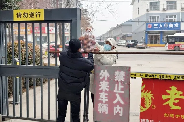 Residents pass fruits across a barrier at a community in Huaxian county in central China's Henan province Wednesday, January 12, 2022. Millions of Chinese are under lockdown in cities under the strict “dynamic zero-case policy” that has allowed China to largely contain major outbreaks, although at considerable cost to local economies. (Photo by Chinatopix via AP Photo)