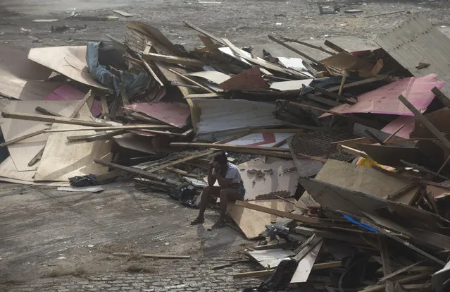 A woman sits on debris from makeshifts homes after an eviction in Rio de Janeiro, Brazil, Friday, April 11, 2014. Squatters in Rio de Janeiro are clashing with police after a Brazilian court ordered that 5,000 people be evicted from abandoned buildings of a telecommunications company. Officers have used tear gas and stun grenades to try to disperse the families. (Photo by Silvia Izquierdo/AP Photo)