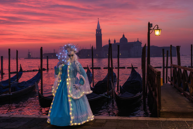A masked masked reveller poses for a sunrise portrait in St. Mark's Square during Venice Carnival 2024 on February 03, 2024 in Venice, Italy. The Venice Carnival began on January 27 and will end on February 13, 2024, and this year is titled “To the East, the wondrous voyage of Marco Polo”. (Photo by Stefano Mazzola/Getty Images)