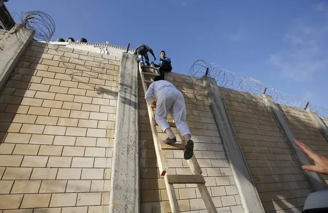 Palestinians, not permitted by Israeli security forces to cross into Jerusalem from the West Bank due to an age limit, climb over a section of the controversial Israeli barrier as they try to make their way to attend the third Friday prayer of Ramadan in Jerusalem's al-Aqsa mosque, in the village of Al-Ram, near Ramallah, July 3, 2015. (Photo by Mohamad Torokman/Reuters)