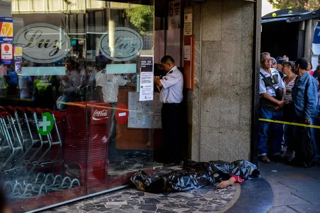 The body of a man lies outside a supermarket, where he died of a heart attack after waiting in a long line to buy food, in Caracas on March 30, 2017. (Photo by Federico Parra/AFP Photo)