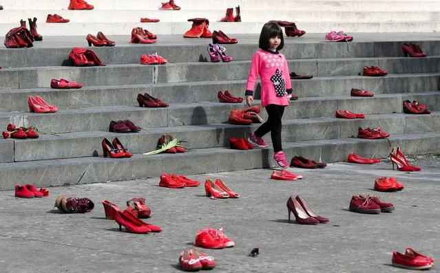 A young girl looks on near an installation of women's red shoes displayed on a staircase, as a symbol to denounce violence against women, in Tirana, Albania, March 8, 2022. (Photo by Florion Goga/Reuters)