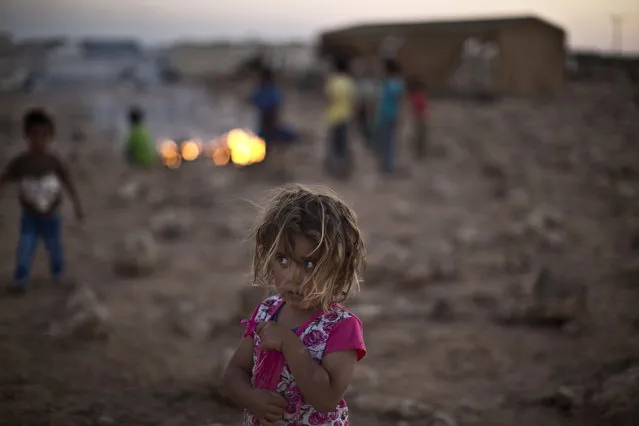 Syrian refugee child Shahd Qadura, 2 1/2, stands by other children burning garbage at an informal tented settlement near the Syrian border on the outskirts of Mafraq, Jordan, Tuesday, July 21, 2015. (Photo by Muhammed Muheisen/AP Photo)
