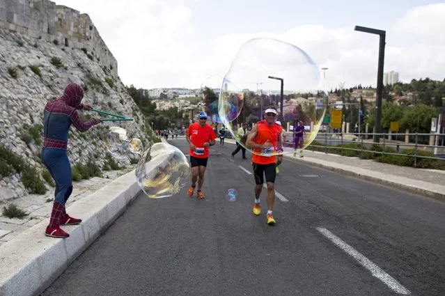 Athletes run onto soap bubbles made by a man dressed in a Spiderman costume as they pass by the Old City walls during the Jerusalem Marathon in Jerusalem, 18 March 2016. (Photo by Abir Sultan/EPA)