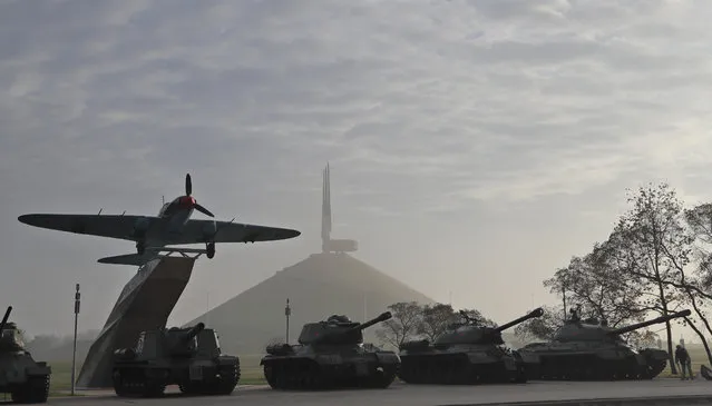 A communal worker, right, cleans the sidewalk next to Soviet era tanks at an open-air WWII museum, with the Mound of Glory war memorial, in the background, on the outskirts of the capital Minsk, Belarus, Tuesday, October 22, 2019. The majestic hill, topped with four rising bayonets, was built in honour of the Soviet liberation of Belarus from Nazi occupation in 1944, and soil for it was brought from nine hero cities of the USSR and from the fields of the most fierce battles of the war. (Photo by Sergei Grits/AP Photo)