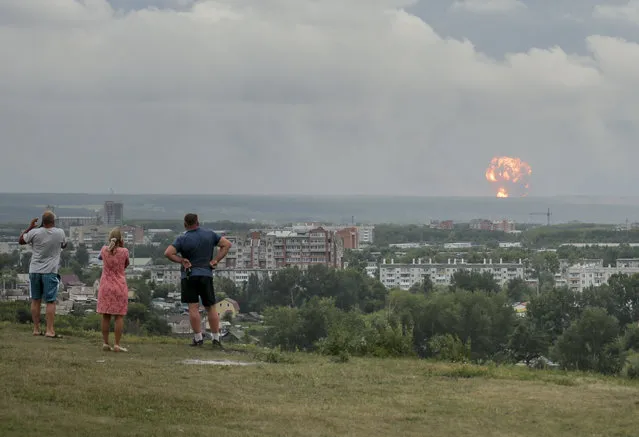 In this photo taken on Monday, August 5, 2019, people watch and photograph explosions at a military ammunition depot near the city of Achinsk in eastern Siberia's Krasnoyarsk region, in Achinsk, Russia. Russian officials say powerful explosions at a military depot in Siberia left 12 people injured and one missing and forced over 16,500 people to leave their homes. (Photo by Dmitry Dub/AP Photo)