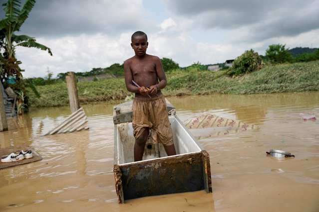 Patricio Perea, 9, stands on a floating refrigerator while holding a few school supplies he managed to salvage after his family home was flooded and destroyed due to heavy rains, in Esmeraldas, Ecuador on June 5, 2023. (Photo by Santiago Arcos/Reuters)