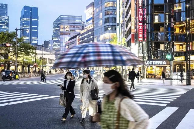 Women cross a street at dusk in Tokyo on April 21, 2022. (Photo by Charly Triballeau/AFP Photo)