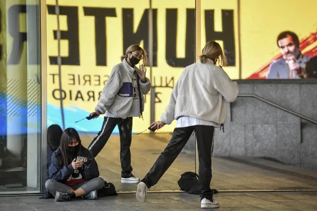 Girls wearing face masks are reflected on a window in downtown Milan's Gae Aulenti square Wednesday, February 26, 2020. The viral outbreak that began in China and has infected more than 80,000 people globally, so far caused 374 cases and 12 deaths in Italy, according to the last figures released by civil protection. (Photo by Claudio Furlan/LaPresse via AP Photo)