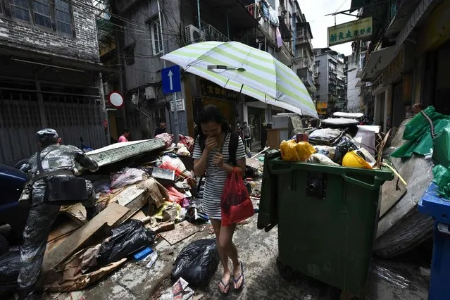 A resident holds her nose due to the smell of rotting debris and garbage as a Chinese People's Liberation Army soldier (L) based at a barracks in Macau helps clear debris from a street in Macau on August 25, 2017, two days after Typhoon Hato hit the territory. At least nine people are now known to have died in Macau when a huge typhoon swept through the gambling hub, plunging casinos into darkness and sparking destructive floods. (Photo by Anthony Wallace/AFP Photo)